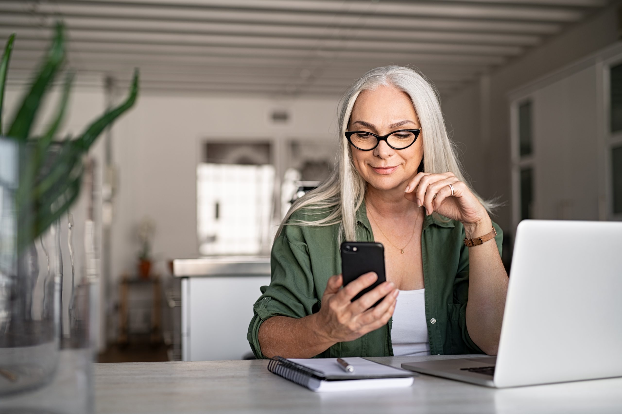 A woman checks her mobile phone while using a laptop