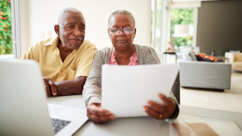 A couple looks over a letter in front of a laptop at their home