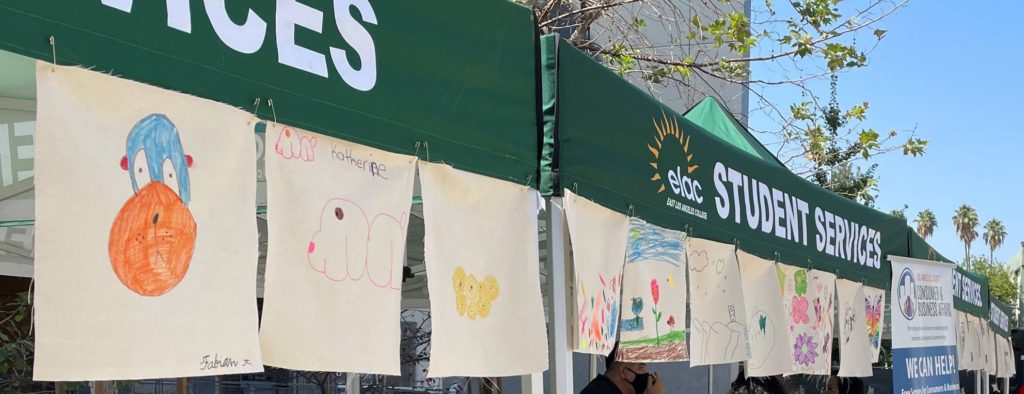 Children's artwork hangs from green canopies at a recent community event