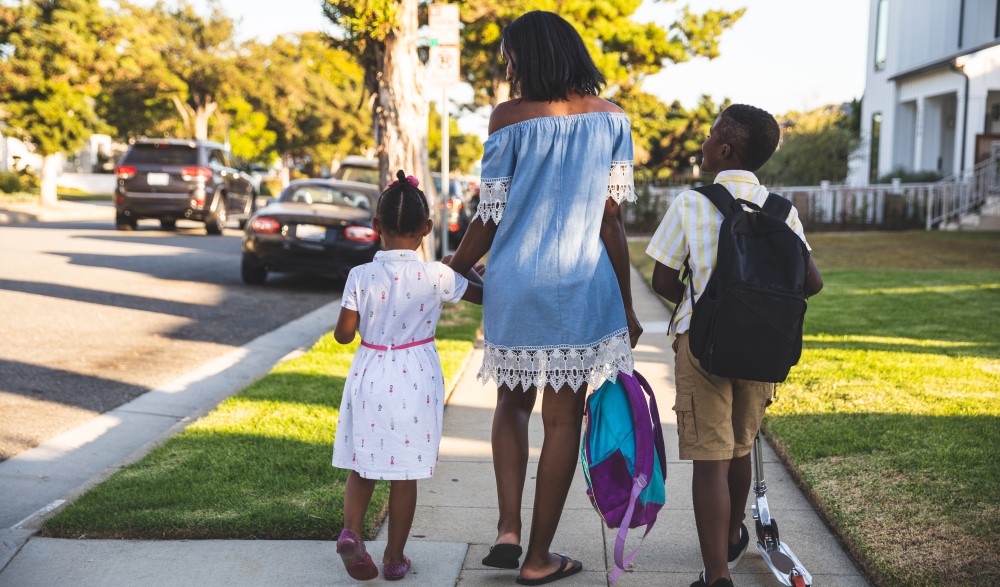 A mother with two young children head off to school with backpacks in tow