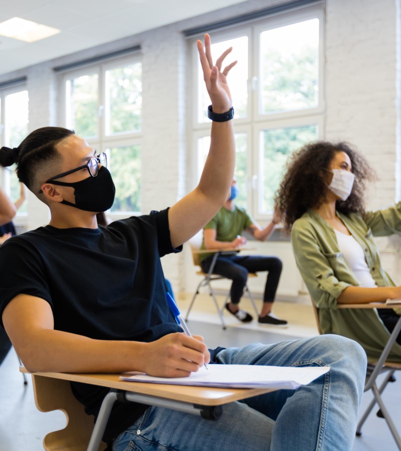 College students in a classroom raise their hands