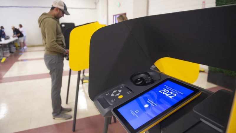 A polling location in LA County with a digital voting device and a voter in the background