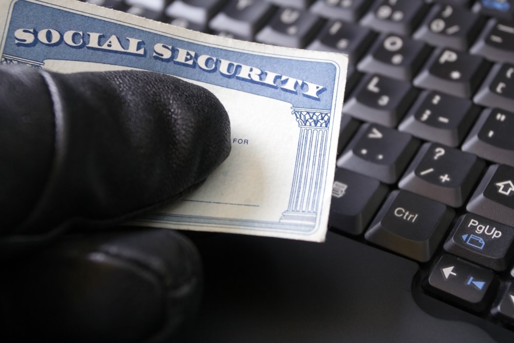 An identity thief with black-gloved hand holds a Social Security card in front of a computer keyboard