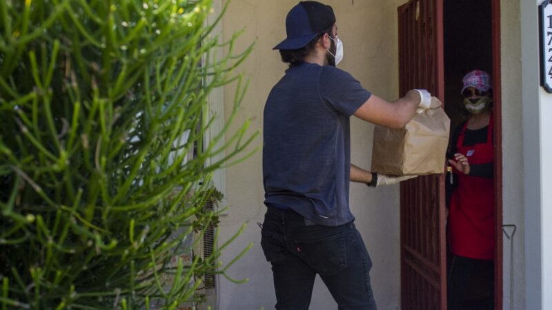A delivery driver drops off a bag of food to person waiting at their front door