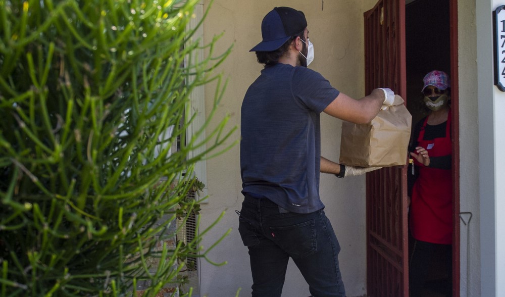A delivery driver drops off a bag of food to person waiting at their front door