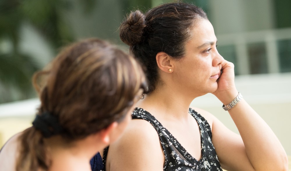 a woman with a worried face rests her head in her hand while another woman looks at her